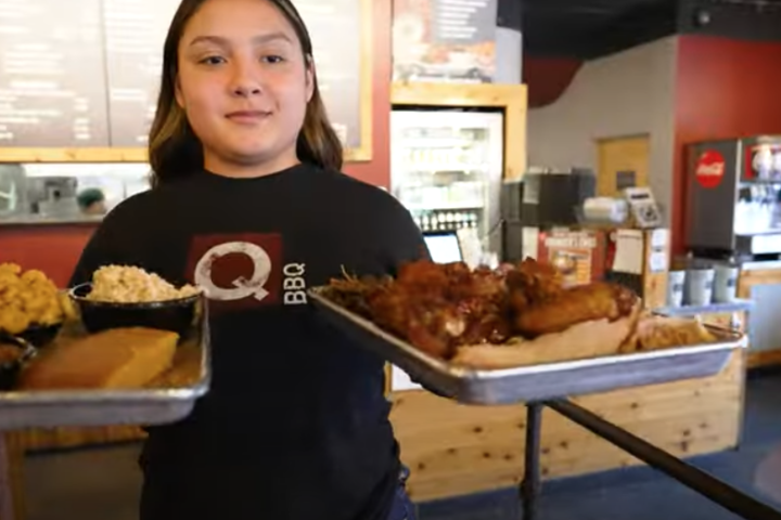 A waitress from Q BBQ in La Grange, IL brings two trays of BBQ towards the foreground of a photo